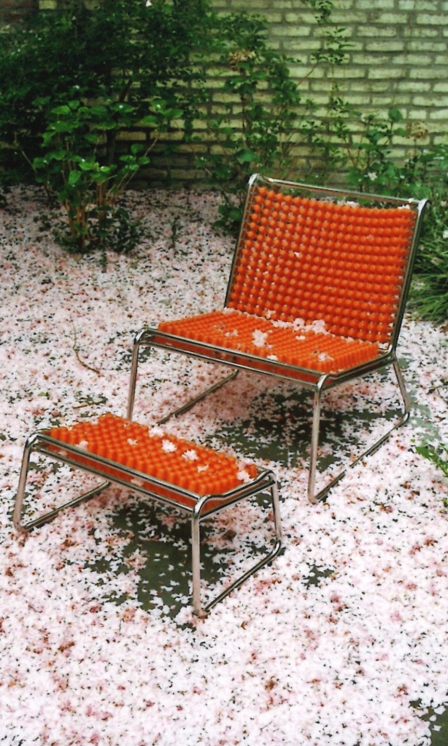 Orangefarbener Stuhl in einem Garten, umgeben von Kirschblütenblättern
