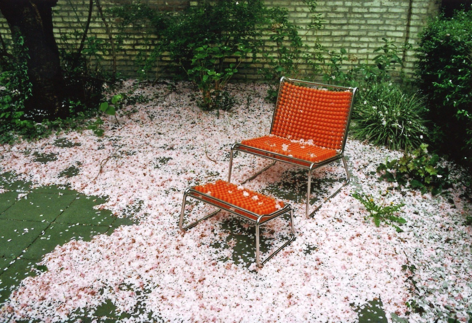 Stehende Figur zwischen Kirschblüten und orangefarbenem Stuhl