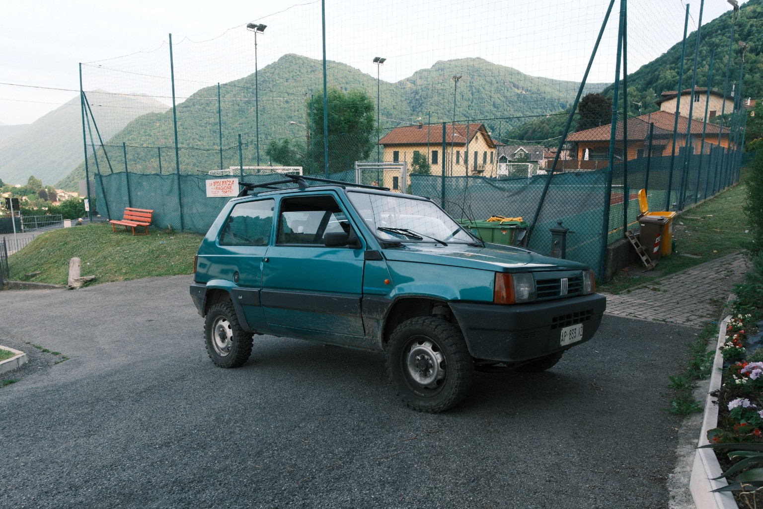 Grüner Fiat Panda vor Sportplatz und Bergen